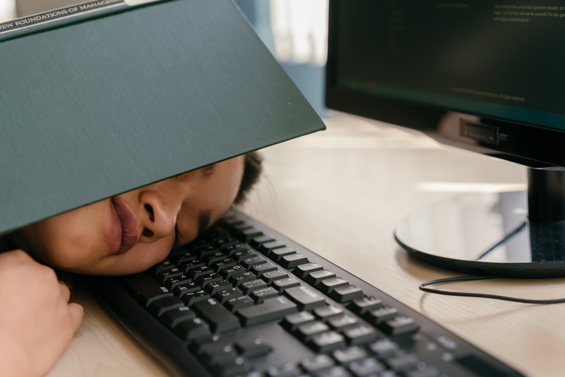 person sleeping on a computer keyboard with an open book covering their face