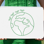 person in green dress in a field holding a lapboard with drawing of the world on it